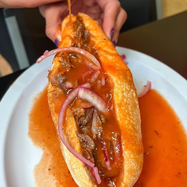 Hands pour orange sauce over a torta ahogada filled with meat and pickled red onions.