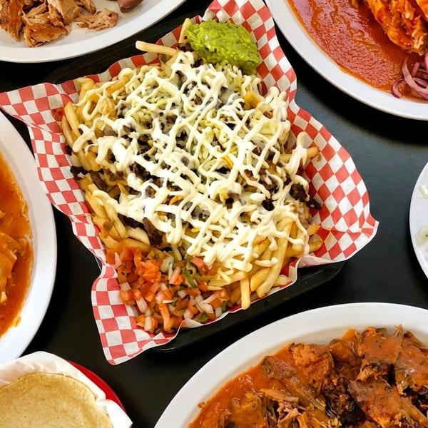 A table laden with various Mexican dishes, including loaded fries, enchiladas, and meat plates.