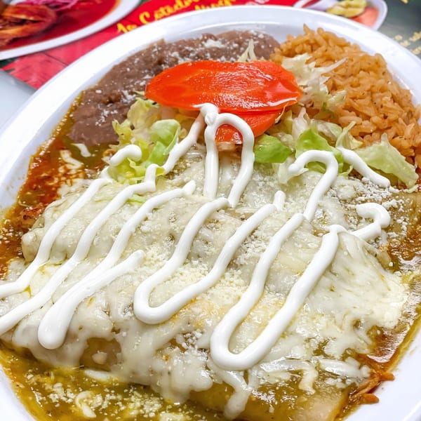 A plate of enchiladas verdes topped with sour cream, lettuce, tomato, rice, and beans.