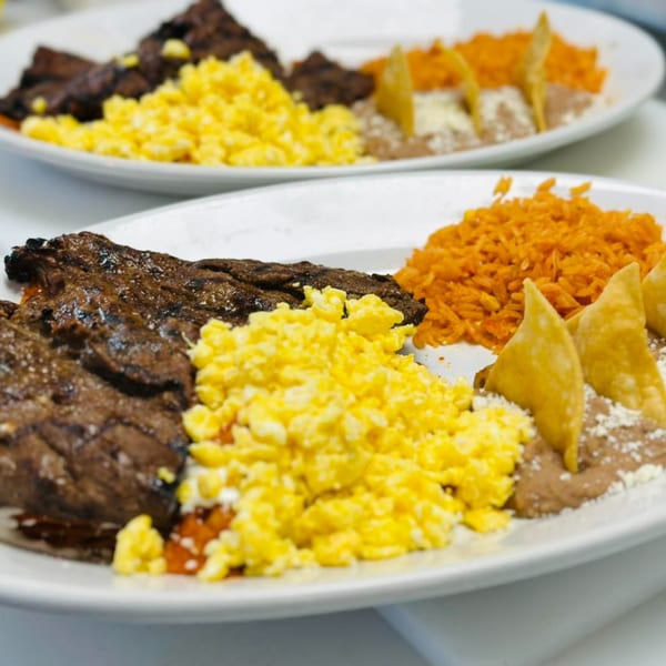 Two plates of carne asada, scrambled eggs, rice, refried beans, and tortilla chips.