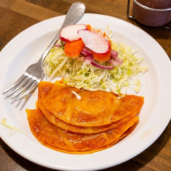Three golden-brown quesadillas with a side of shredded cabbage, radish, and carrots on a white plate.