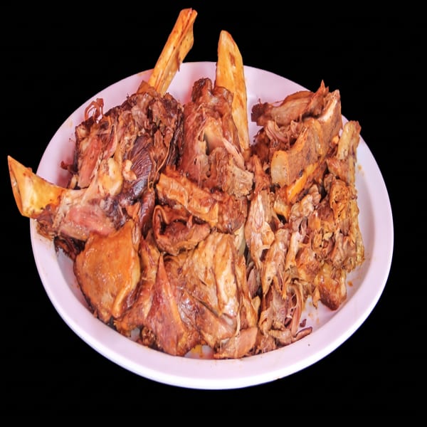 A white plate piled high with succulent, shredded barbacoa meat and bones.